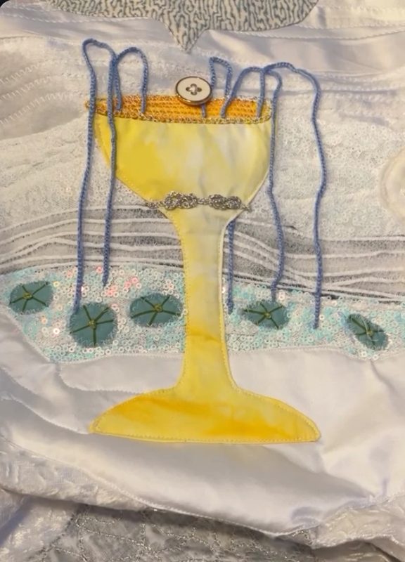 Ace of Cups art quilt: a hand-dyed yellow cup overflowing with blue yarn above sequin water and lily pads