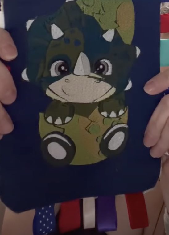 A navy crinkle toy with a baby triceratops print and ribbon tabs